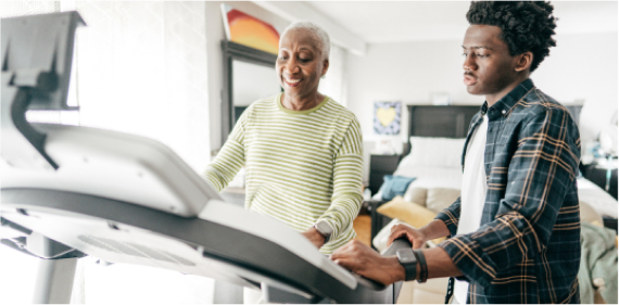 Senior person on treadmill with younger person standing next to it and assisting