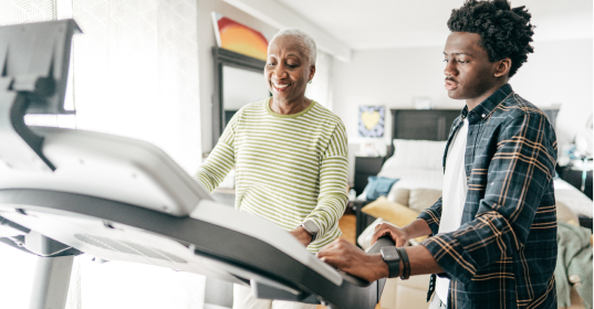 Senior person on treadmill with younger person standing next to it and assisting